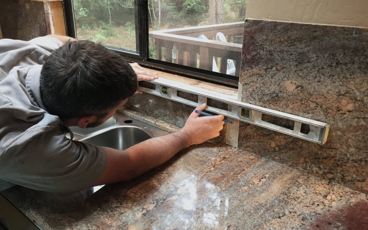 Craftsman checking a granite countertop for level during an install, working carefully along the edge