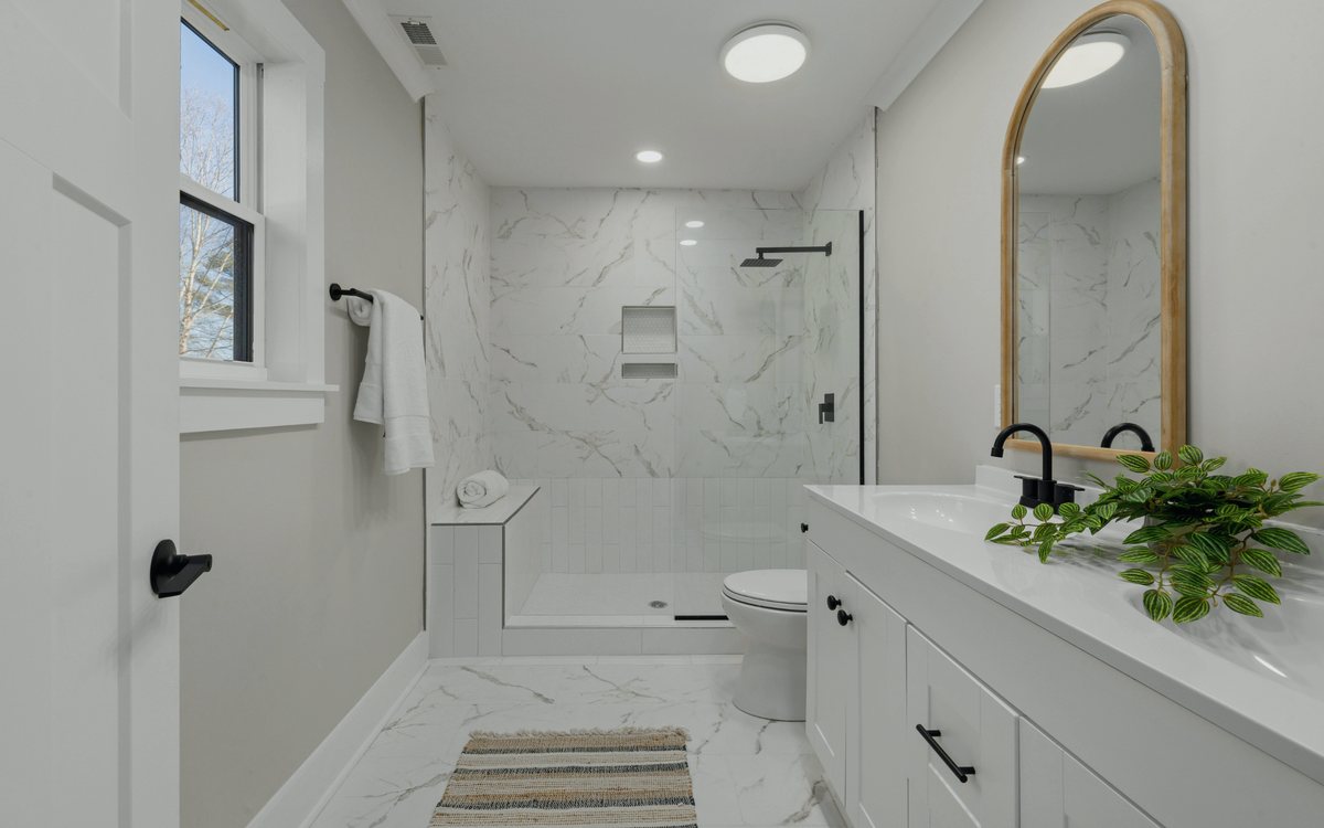 Walk in shower finished in large format marble look porcelain tile with a glass panel, black fixtures, and a built in niche
