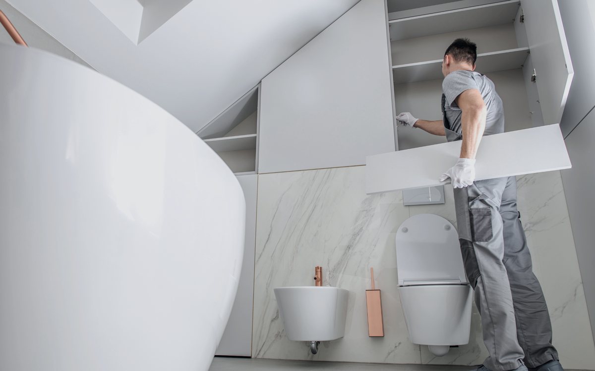 Installer fitting large format wall panels around a wall hung toilet during a bathroom renovation