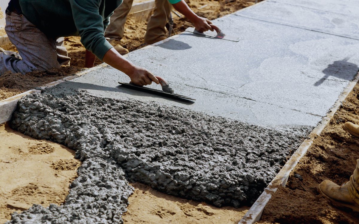 Finisher hand troweling the surface of fresh concrete smooth along a formed edge