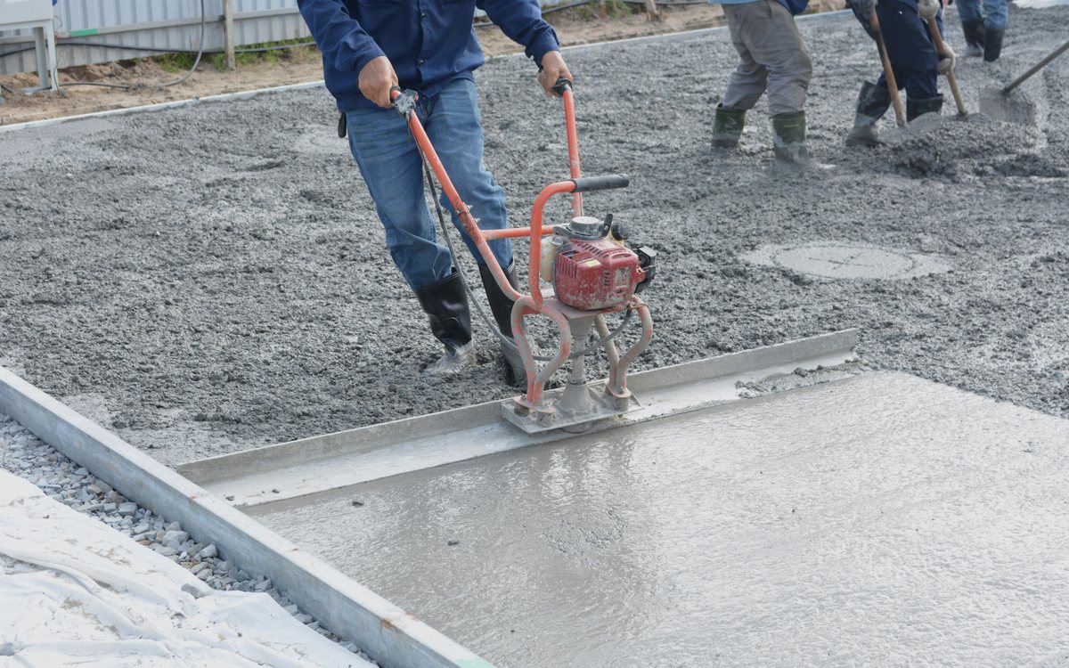Worker screeding a freshly poured concrete slab flat with a power screed before finishing