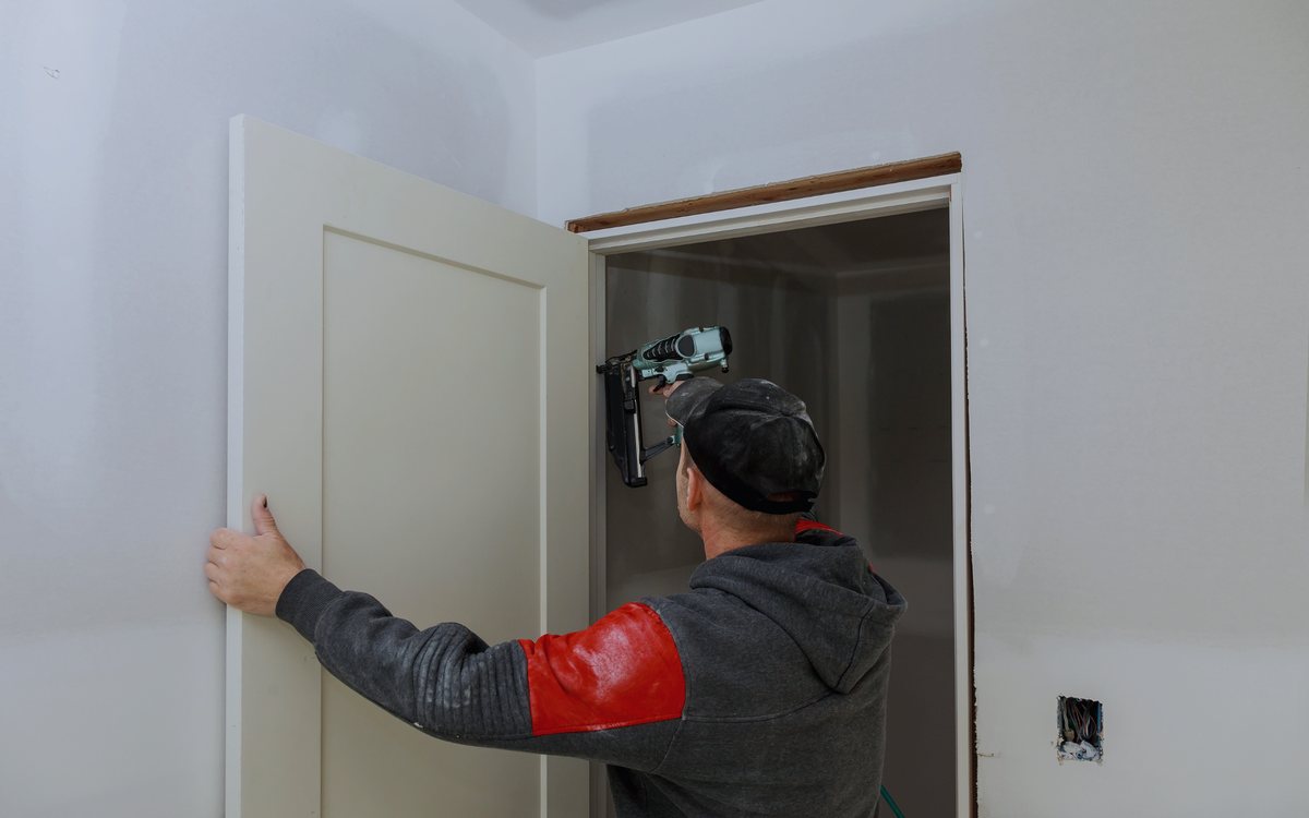 Carpenter hanging a new interior door and checking the reveal along the jamb before fastening the hinges