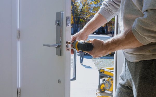 Installer fitting a handleset and latch into a new exterior door, adjusting the hardware so it closes cleanly