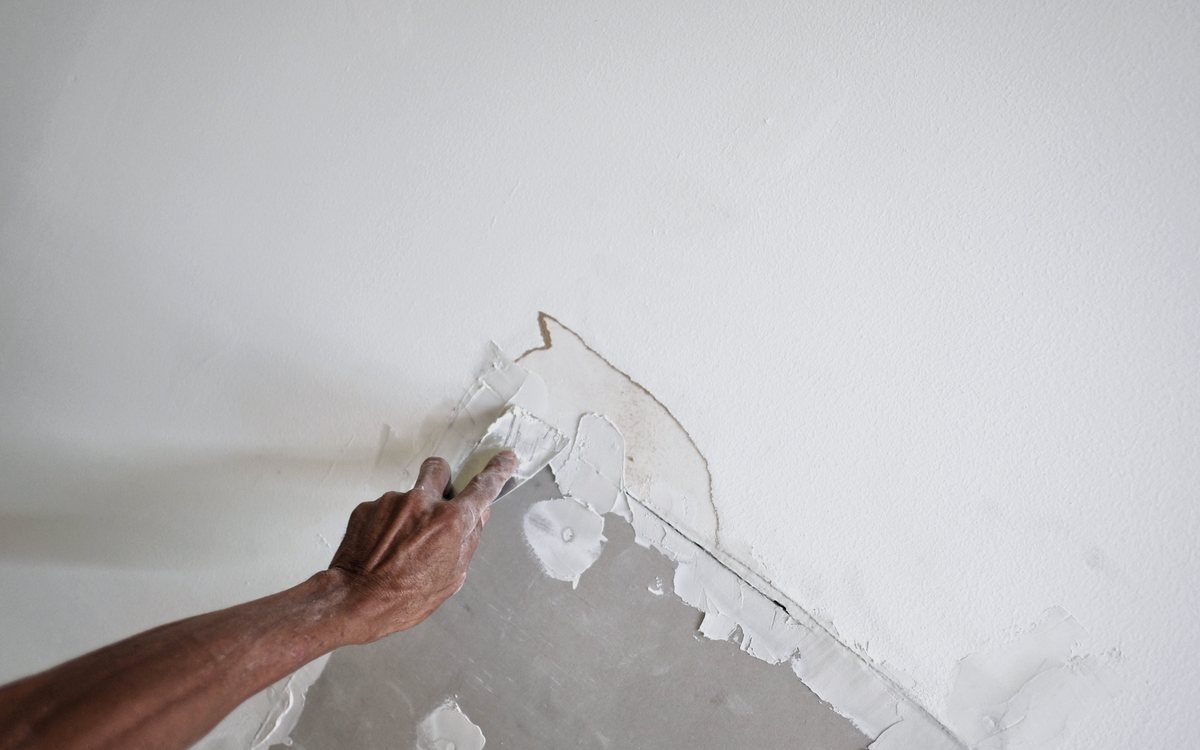 Hand patching a damaged section of wall with joint compound before sanding and texture matching