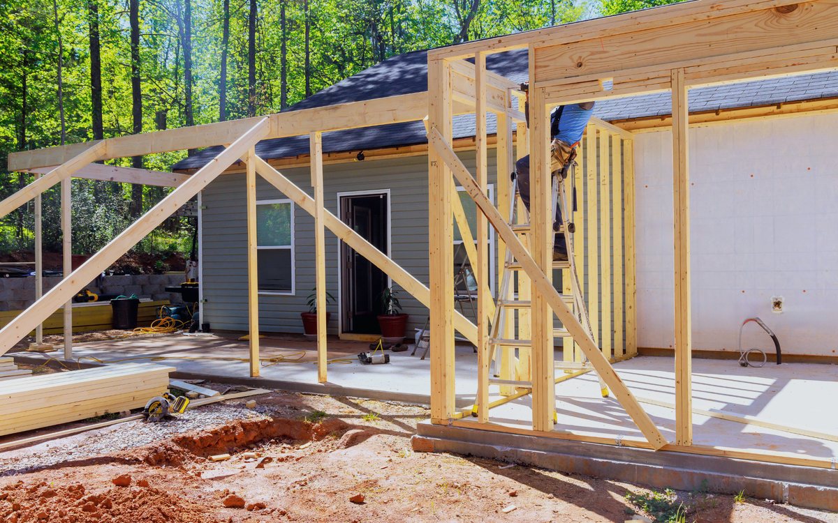 New room addition framed onto the back of a single story house, with roof trusses set and the wall framing exposed