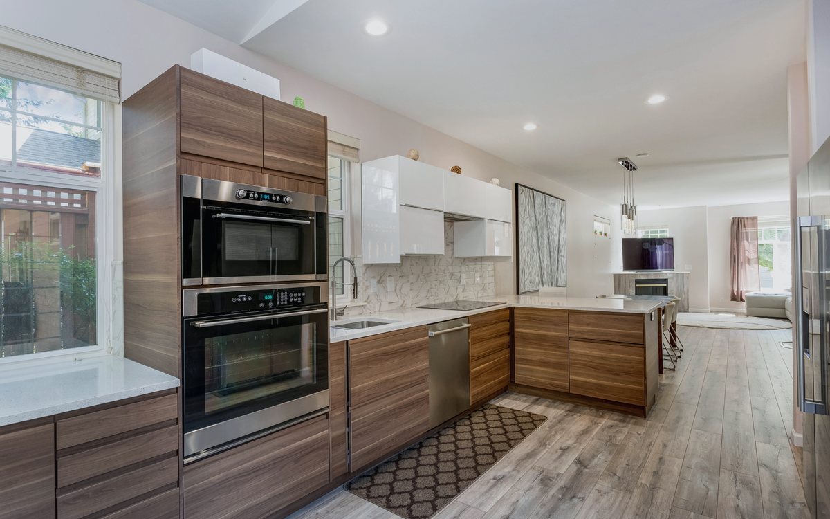 Modern walnut and white kitchen with a built in double wall oven, stainless appliances, and an open sightline to the living room