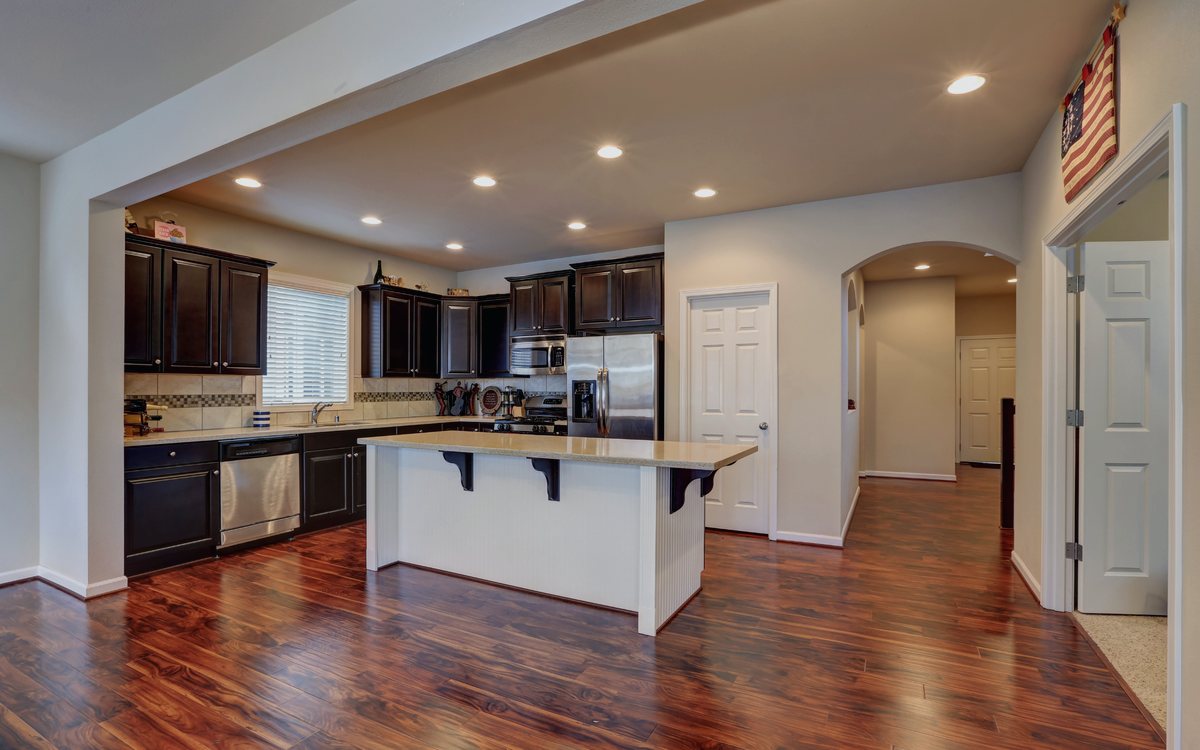 Open concept kitchen with dark stained cabinets, a raised breakfast bar island, and hardwood flooring running through to the entry