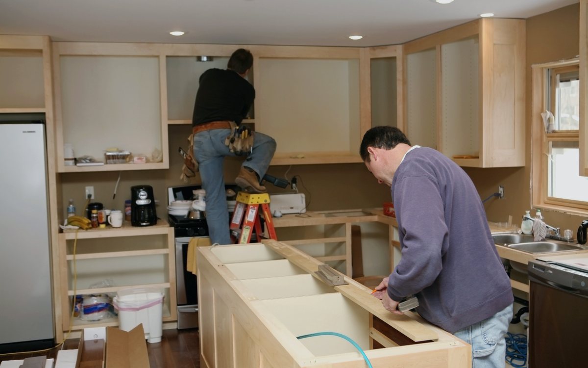 Crew building a kitchen island base and setting cabinet boxes during a full kitchen renovation, with the room still under construction