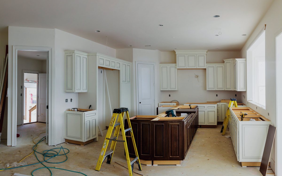 Kitchen mid remodel with new white cabinetry set and a stained island base in place, before countertops and flooring go in
