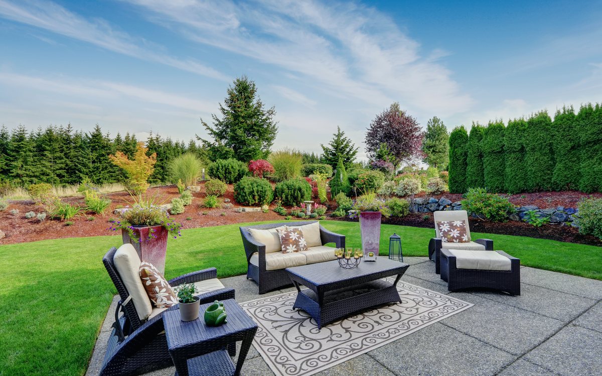 Designed backyard with a paver patio, lounge seating, layered planting beds, and a manicured lawn