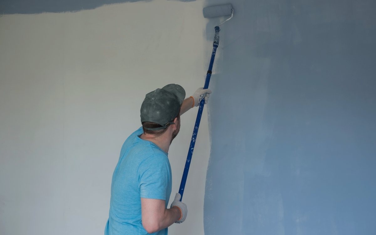 Painter rolling a smooth second coat onto an interior wall with an extension pole