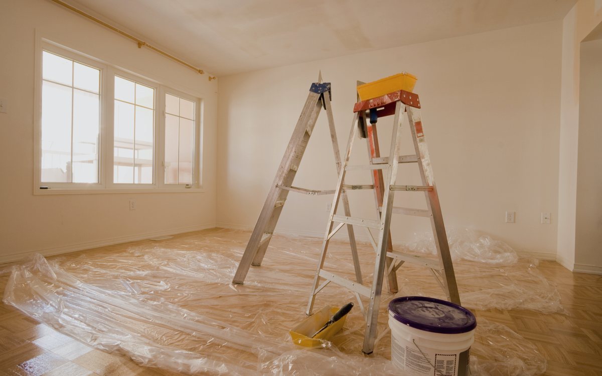Interior room prepped for painting with floors fully covered, a ladder set up, and the walls patched and primed
