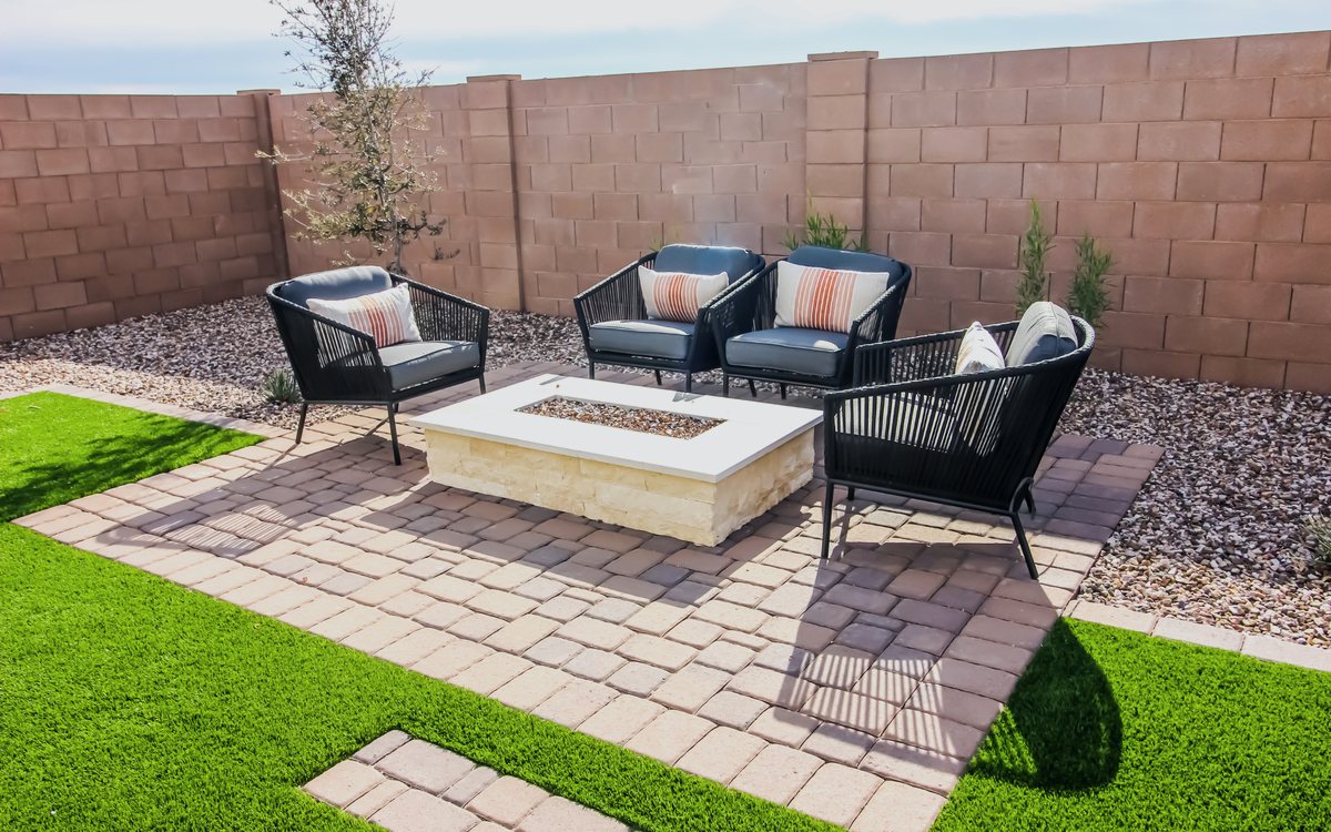 Paver patio with a fire pit and lounge seating set into an artificial turf backyard