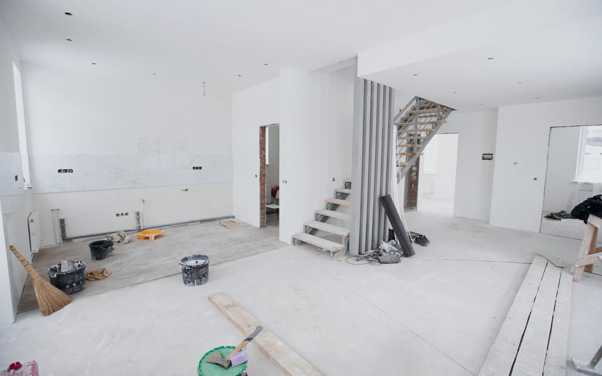Interior of a house mid renovation with a newly framed staircase, fresh drywall, and protective covering over the subfloor