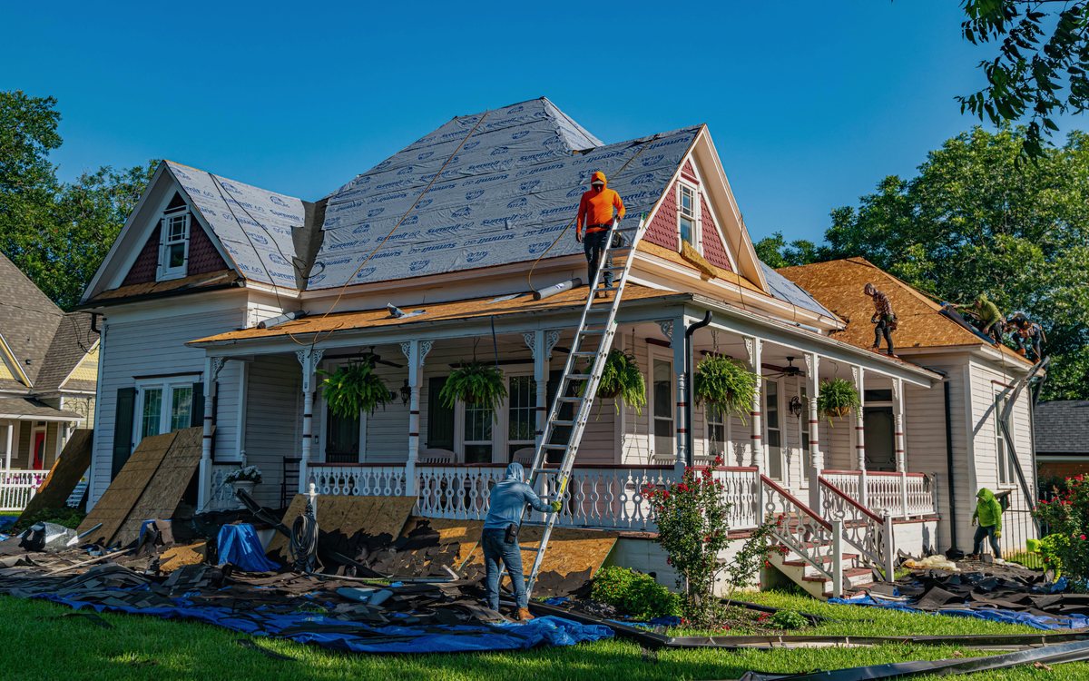Crew reroofing and residing a Victorian home during a whole house renovation, with materials staged across the front lawn