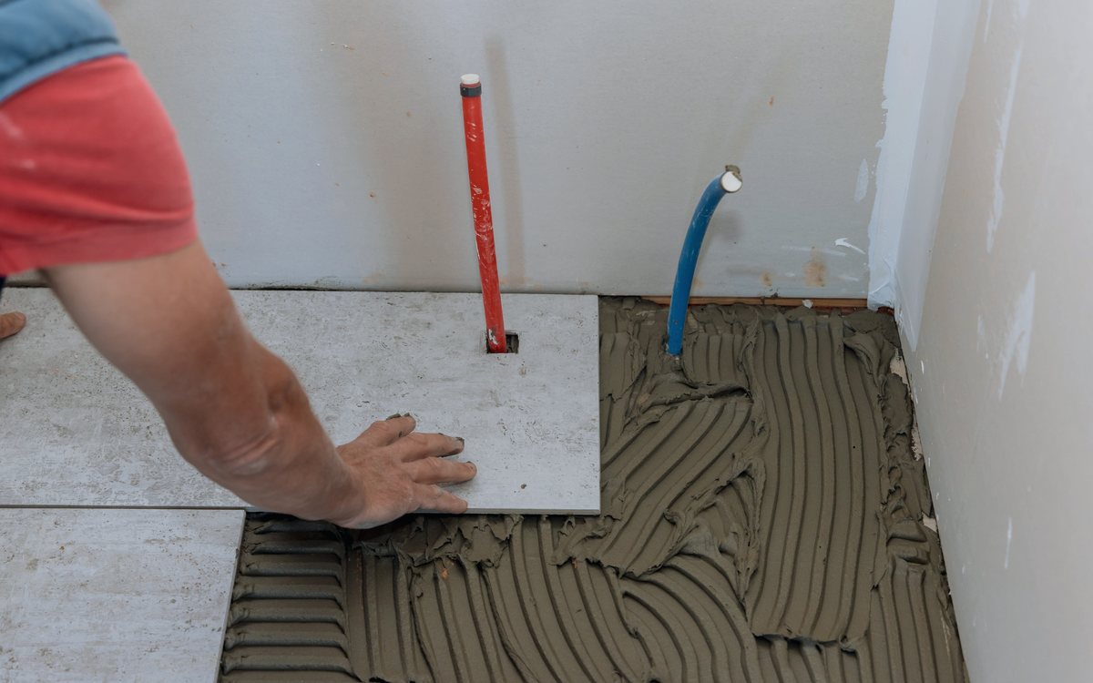 Hands pressing a tile into fresh thinset over a combed mortar bed during a floor tile installation