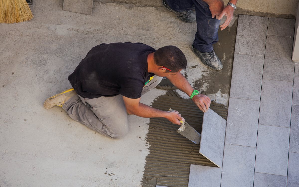 Tile setter combing thinset with a notched trowel and setting floor tile to a straight line