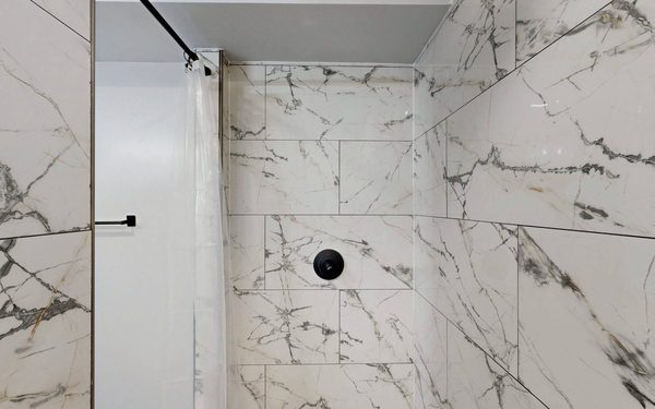 Finished walk in shower tiled floor to ceiling in marble look porcelain with a linear drain and black fixtures