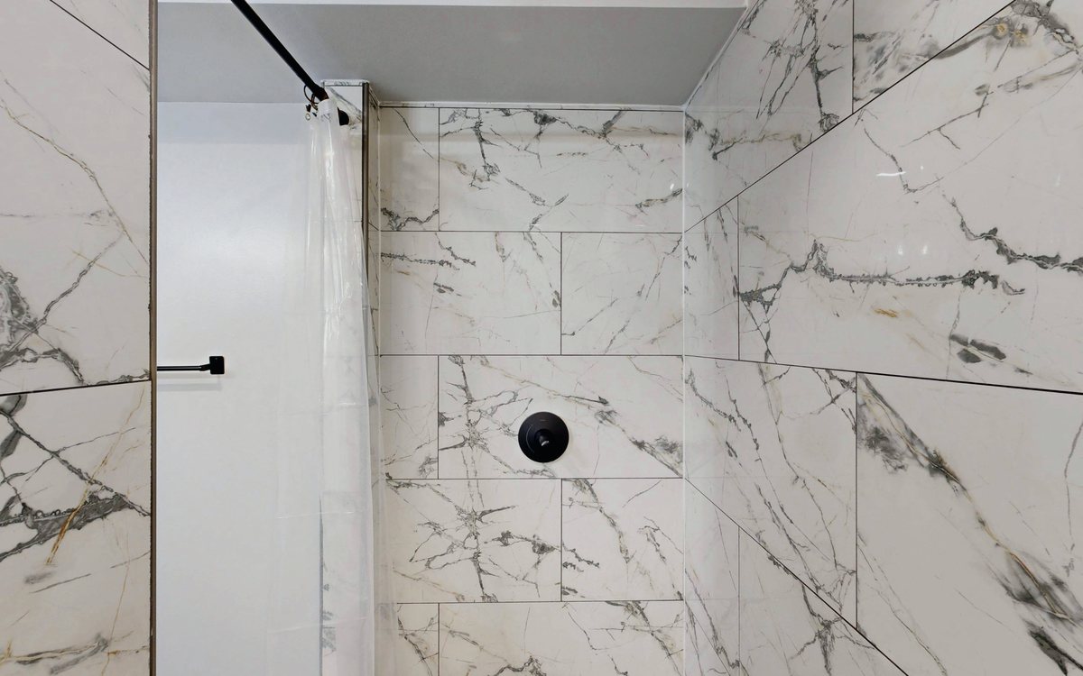 Finished walk in shower tiled floor to ceiling in marble look porcelain with a linear drain and black fixtures